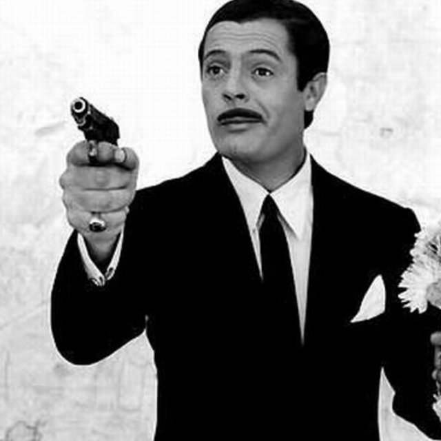 Marcello Mastroianni with a gun in one hand and a flower in the other